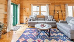 En mysig stuga med en grå soffa, ett runt soffbord och en färgglad matta.