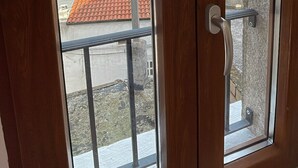 Een houten deur met twee glaspanelen, elk met uitzicht op een dak met rode tegels en een landschap met heuvels en een waterpartij.
