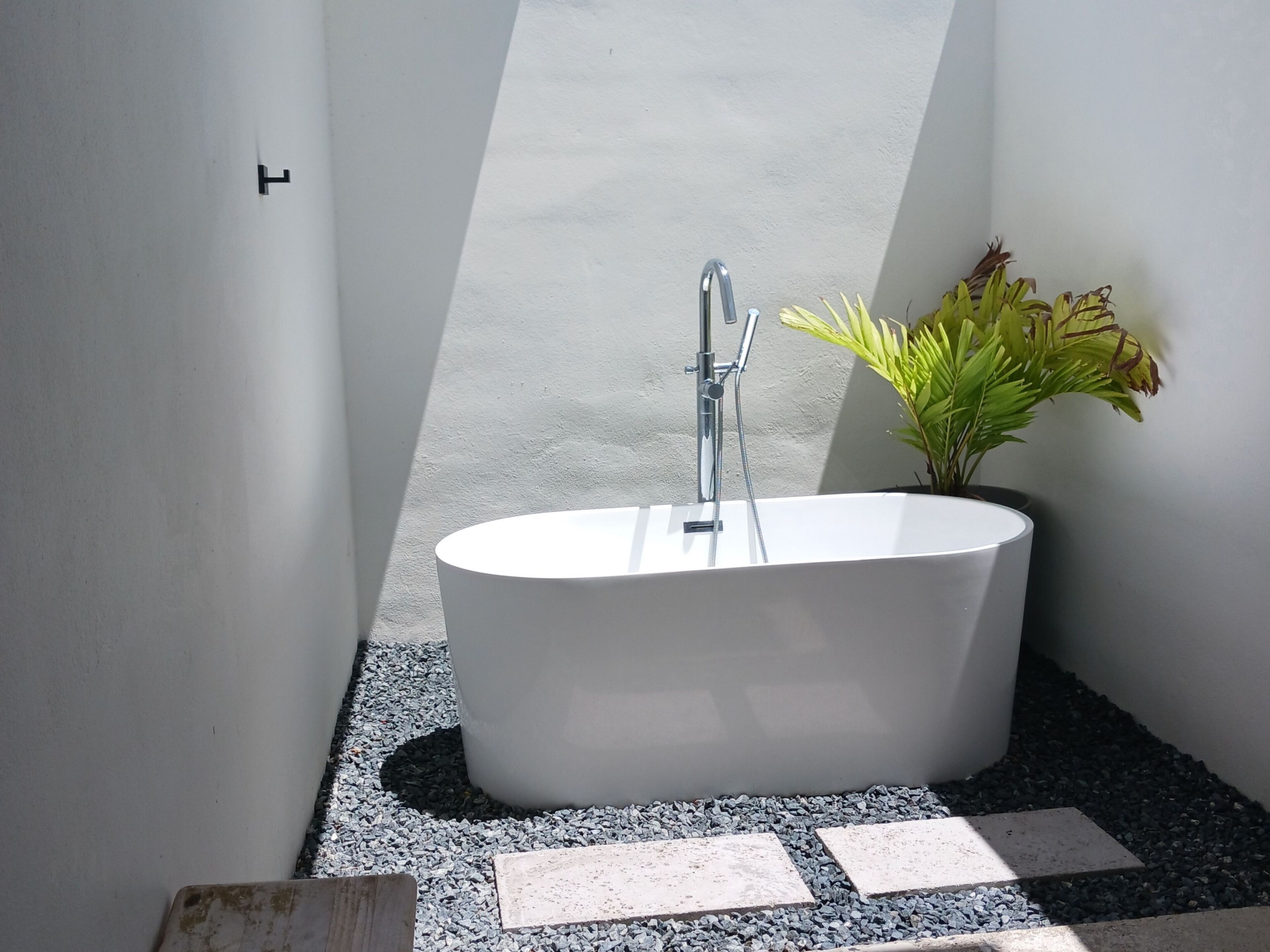 Een moderne badkamer met een vrijstaand bad, douchekop en een potplant.