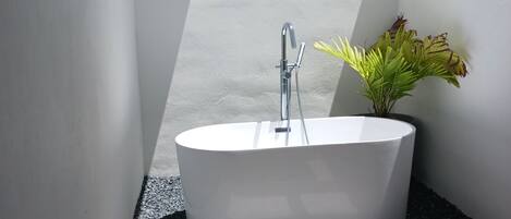 Een moderne badkamer met een vrijstaand bad, douchekop en een potplant.