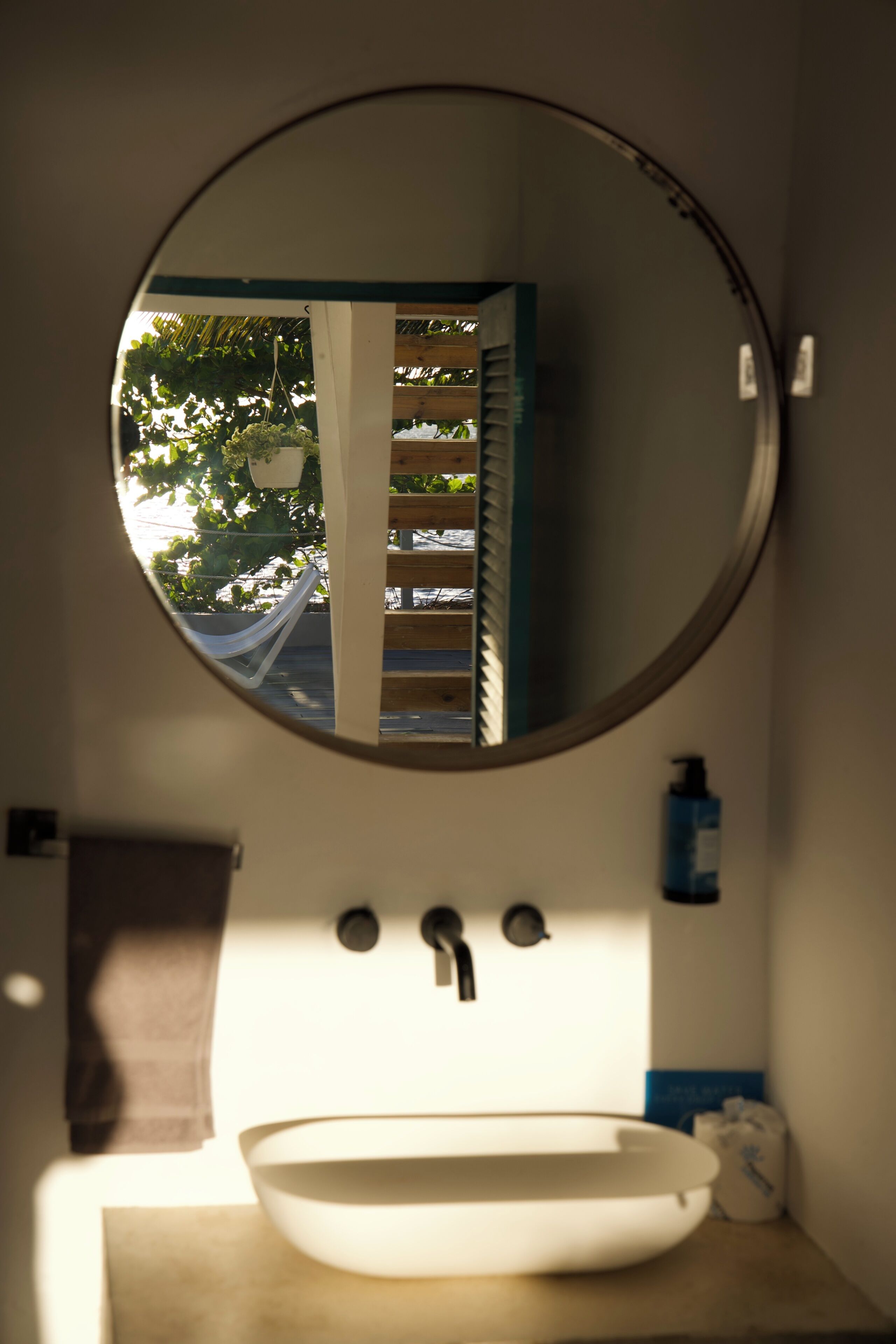 Une salle de bain avec un miroir rond, un lavabo blanc et un porte-serviettes.
