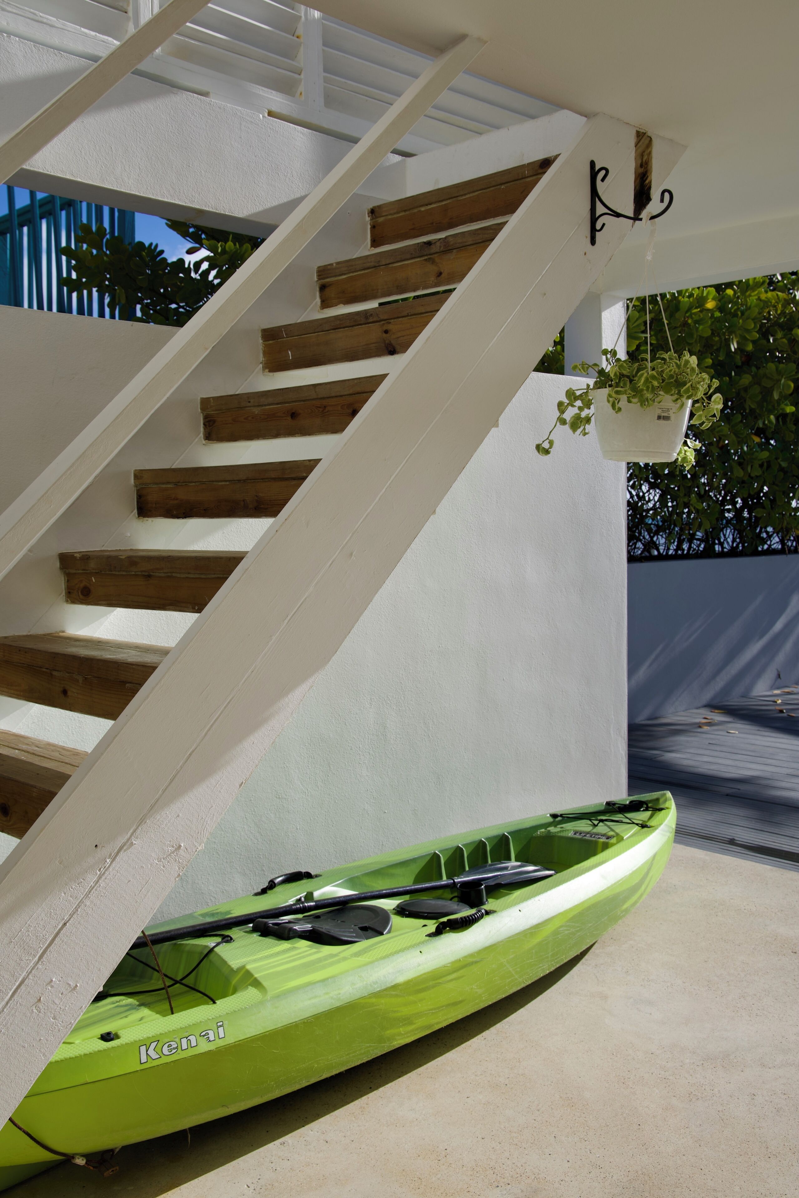 A green kayak with 'Kenai' written on it, positioned under a staircase with white walls and wooden steps.
