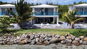 A clear water body with a kayaker, a white building with blue railings, and a stone wall. - Picuas Village (Río Grande)