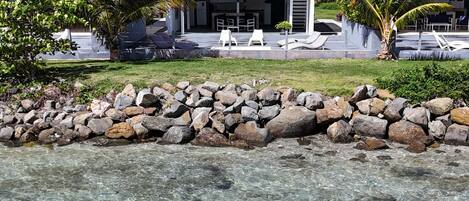 A clear water body with a kayaker, a white building with blue railings, and a stone wall.