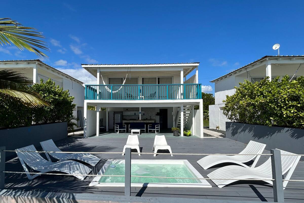 A two-story building with a balcony, a pool area with lounge chairs, and a kitchen visible inside.