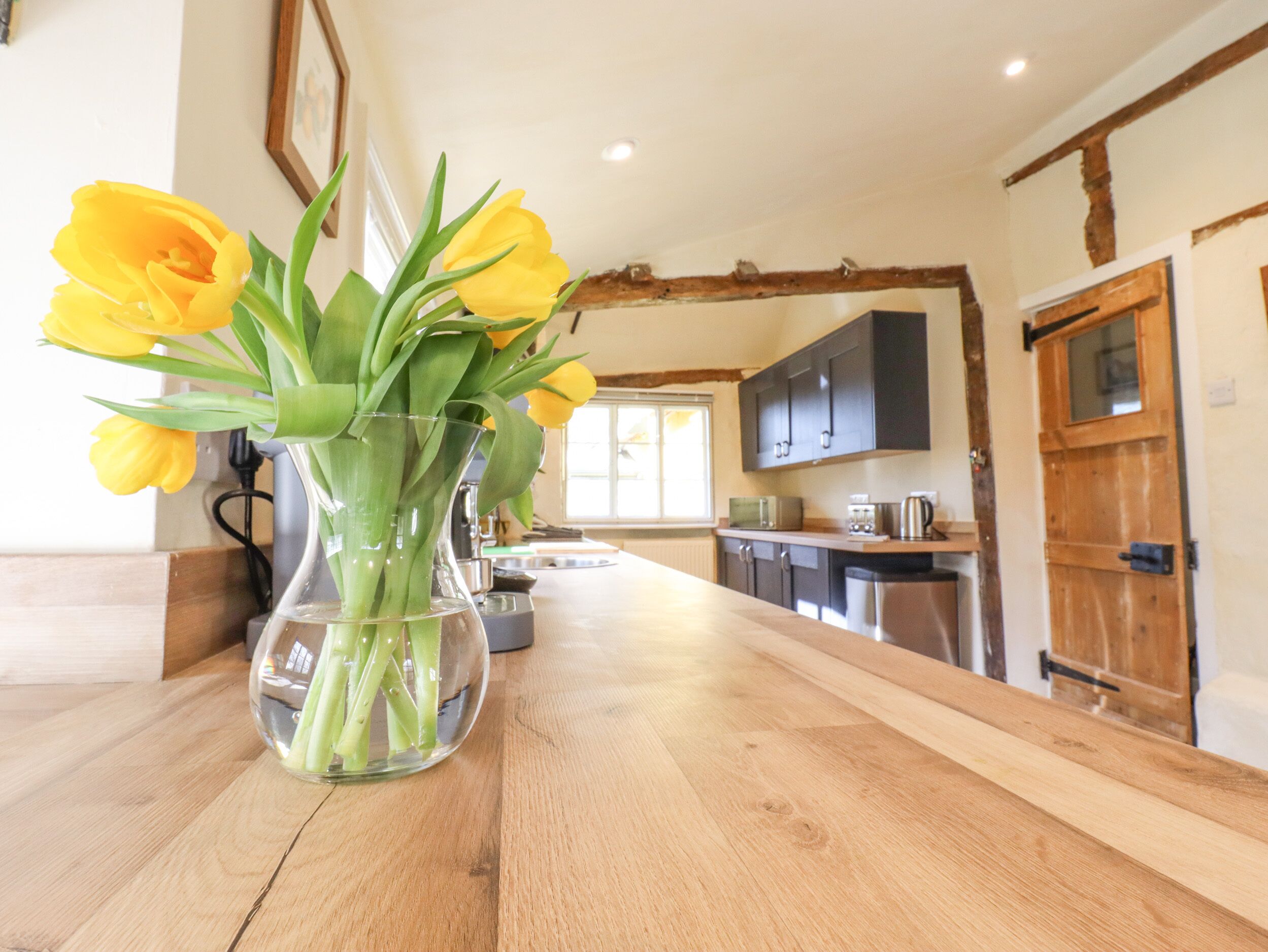 A kitchen with wooden beams, a wooden door, and a vase with yellow flowers on a wooden countertop.