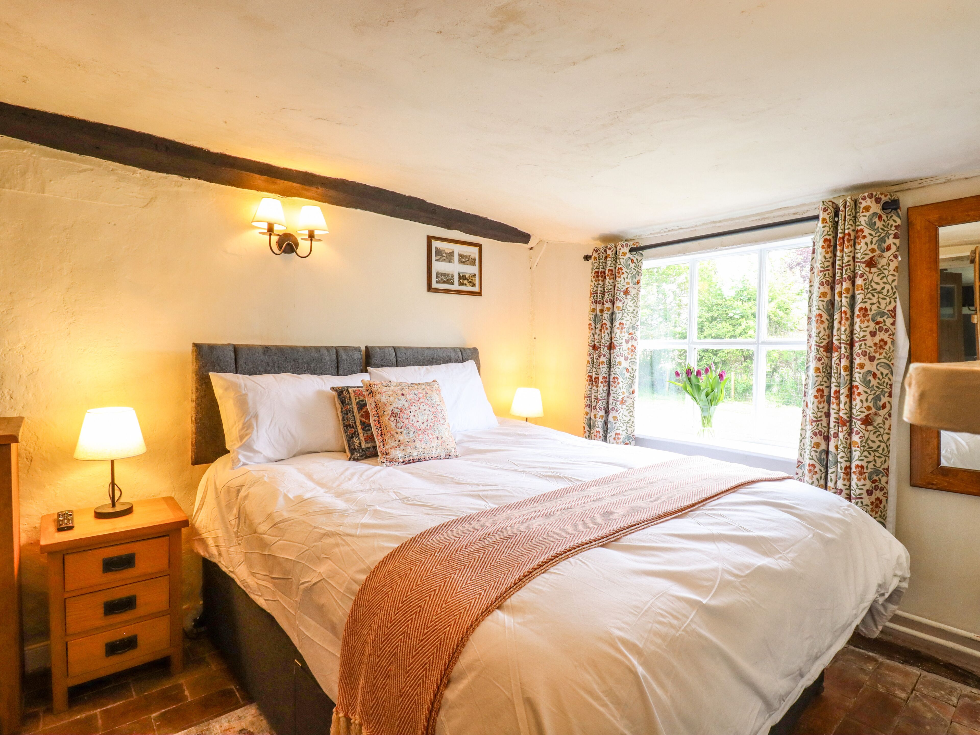 A bedroom with a bed, two bedside tables, a nightstand, a window with curtains, and a wall-mounted picture.