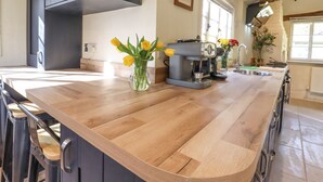 A kitchen with a wooden countertop, a coffee machine, and a vase with flowers. - The Abbey Cottage (Bury St Edmunds)