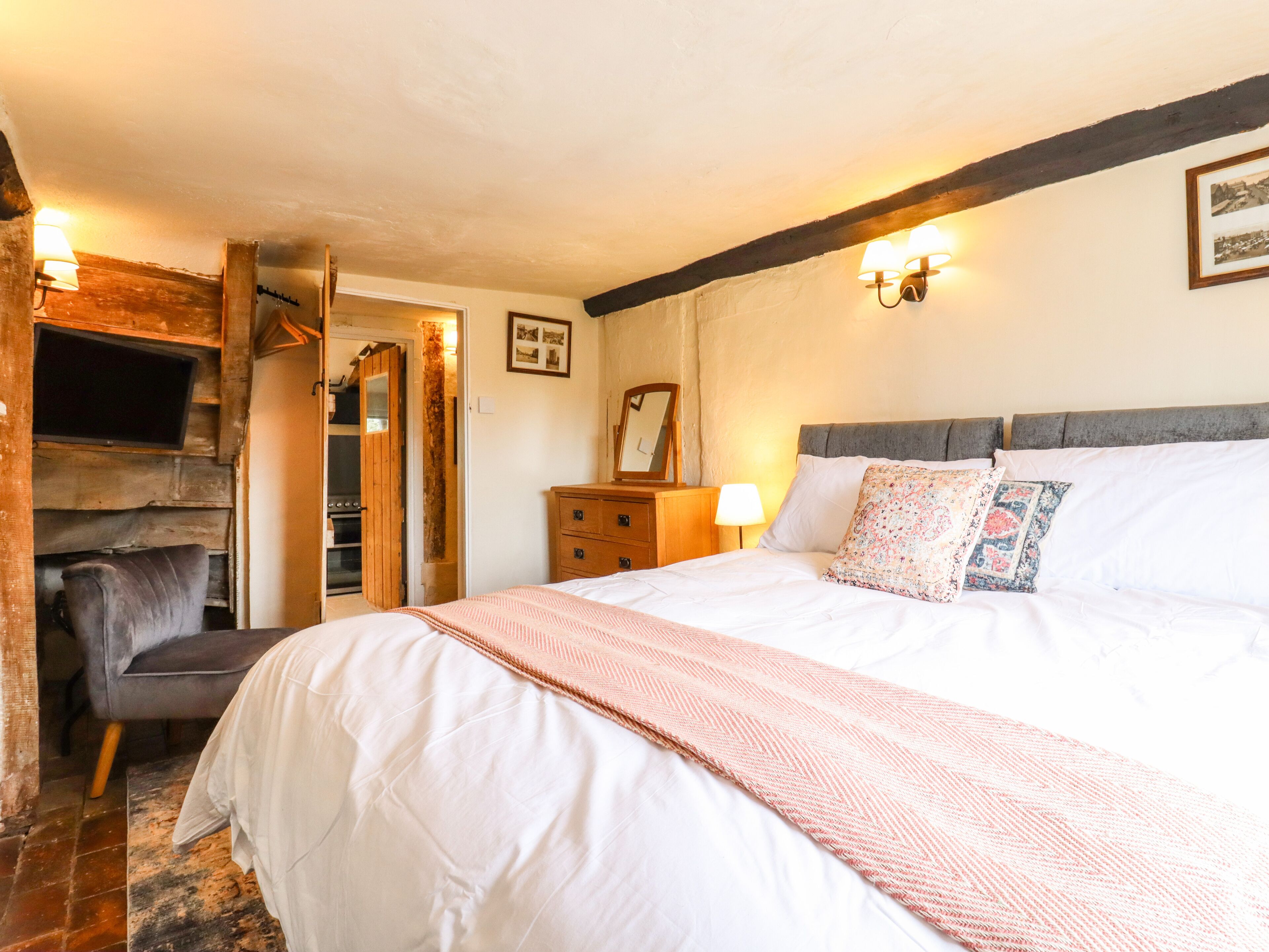 A bedroom with a large bed, a dresser, a mirror, a television, and a fireplace.