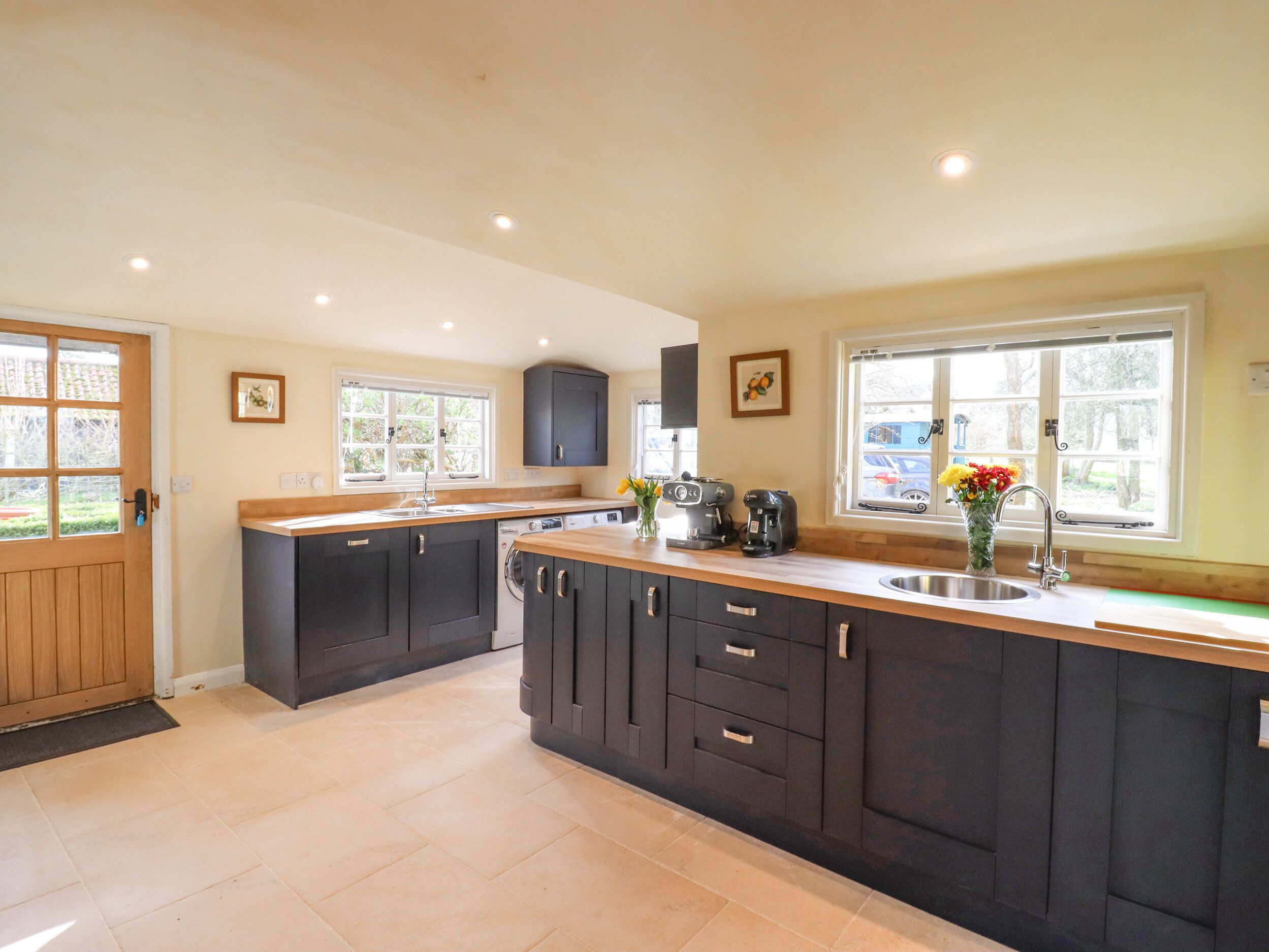 A modern kitchen with dark cabinetry, a wooden countertop, and a built-in dishwasher.