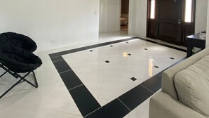 Un ampio soggiorno con un grande pavimento a scacchi bianconero, una poltrona nera e un divano color beige.