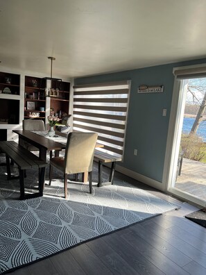 A dining area with a table, chairs, a bench, a patterned rug, and a view of the outdoors.