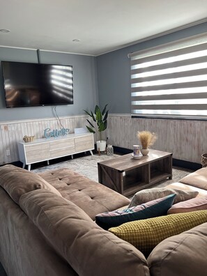 A living room with a large flat-screen TV, a white cabinet, a wooden coffee table, and a beige sofa.