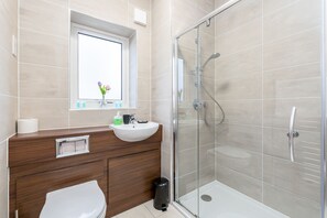 A bathroom with a white sink, mirror, and toilet. It has beige tiles and a glass shower enclosure. - 2BR Apt-sleeps 5-accessible-central Dartford (Dartford)