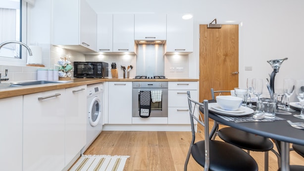 Une cuisine moderne avec des meubles blancs, un lave-linge, un four et un coin repas avec une table dressée pour quatre personnes.