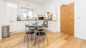 Une cuisine moderne avec des meubles blancs, une porte en bois et un coin repas comprenant une table et des chaises.