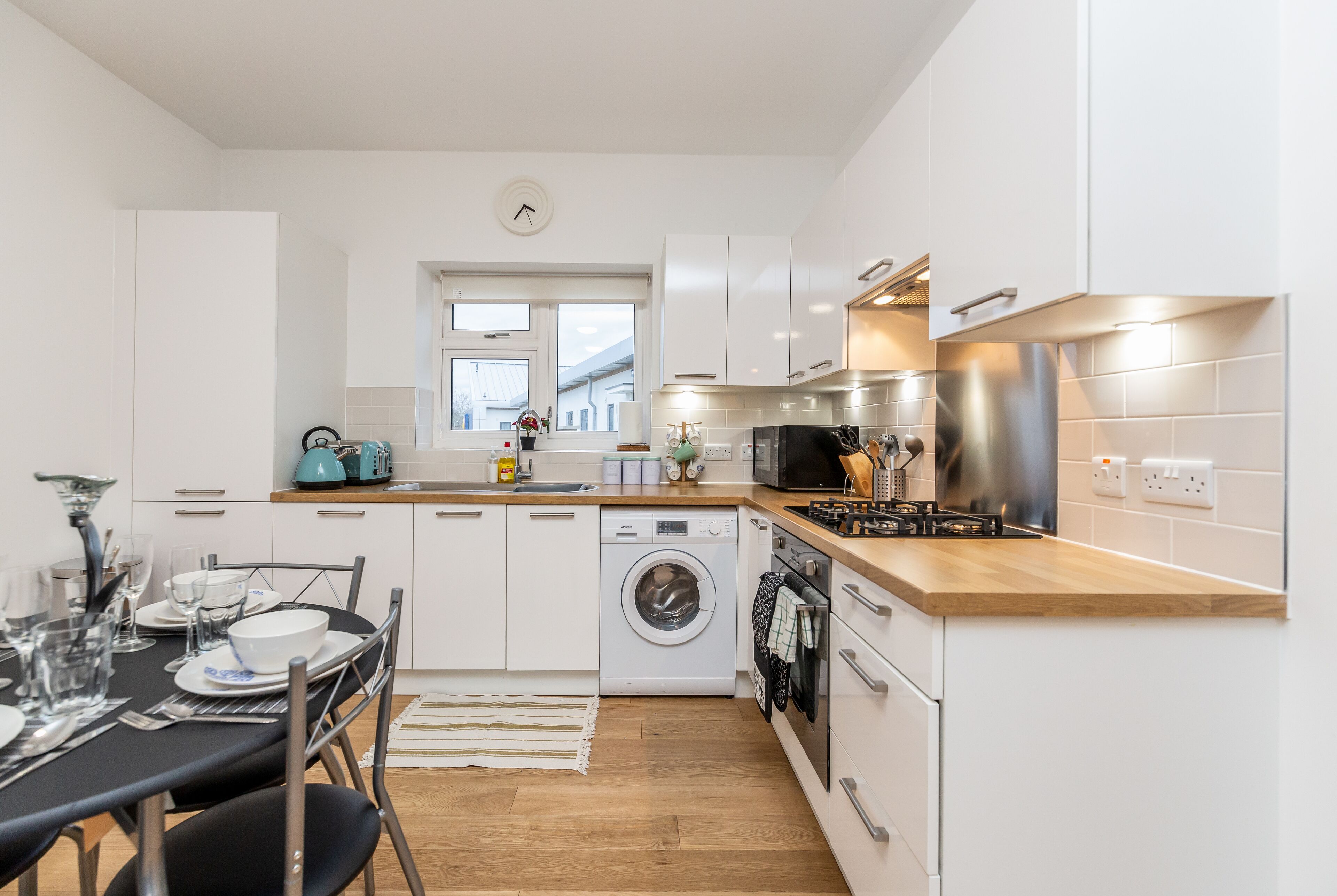 A modern kitchen with white cabinets, a washing machine, a microwave, and a sink.