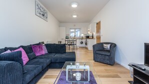 Un salon moderne avec un canapé d’angle, une table basse en verre et un fauteuil gris.