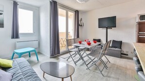 Una sala de estar moderna con comedor, un sofá, una mesita y un televisor instalado en la pared.