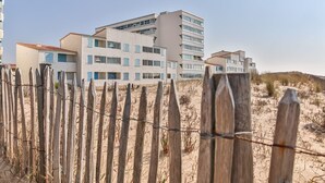 Un hotel frente a la playa con varios pisos, una playa arenosa en primer plano y un cielo despejado.