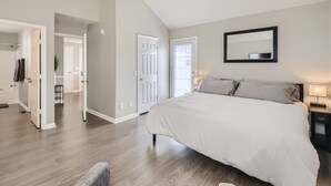 A bedroom with a large bed, a ceiling fan, a mirror, and a door leading to another room.