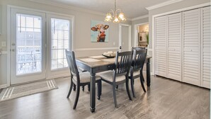 A dining area with a wooden table, four chairs, a chandelier, and a painting on the wall.