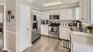 A modern kitchen with white cabinetry, stainless steel appliances, and a wooden floor.