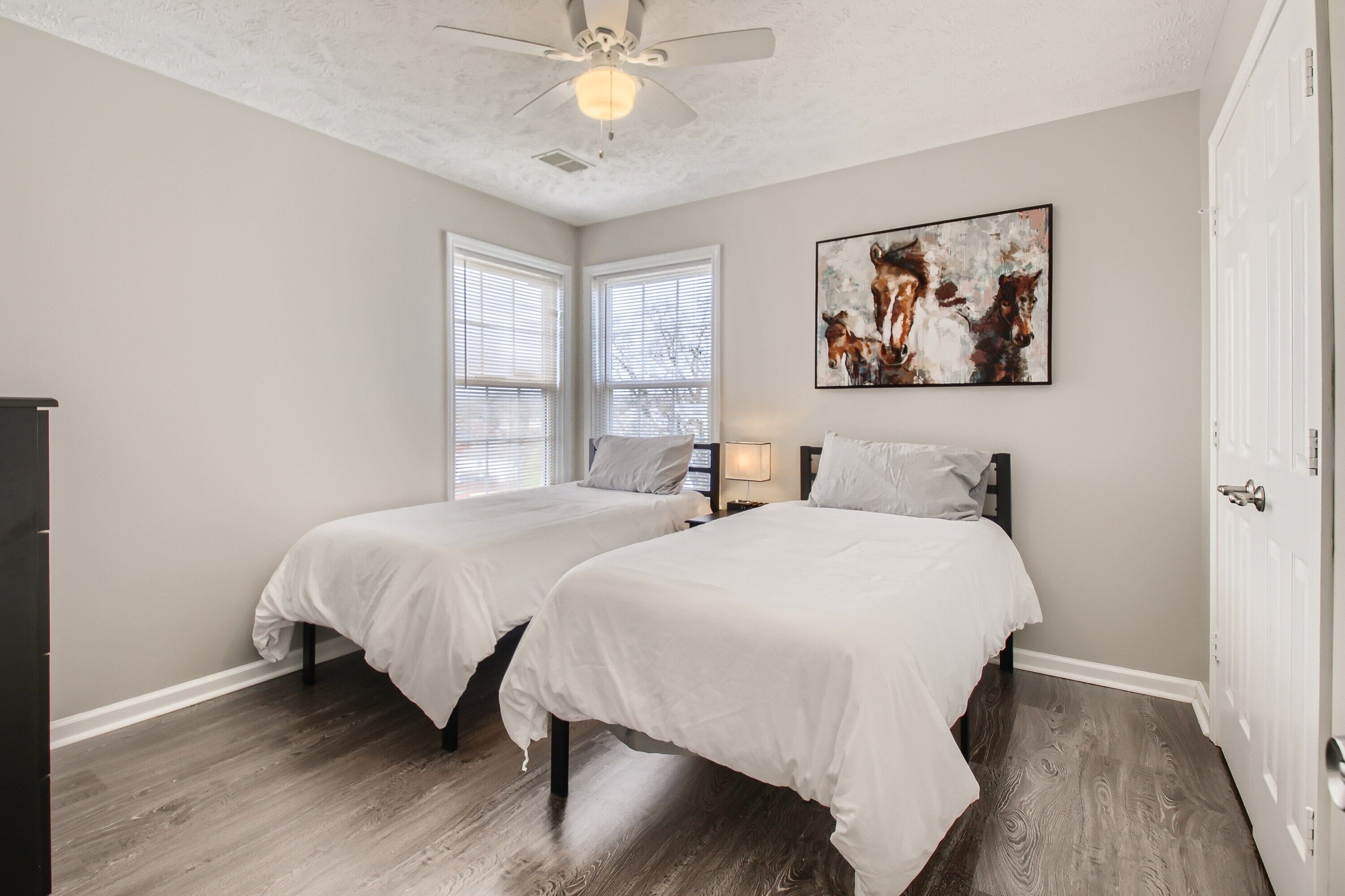 A bedroom with two beds, a ceiling fan, and a painting on the wall.