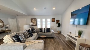 A modern living room with a grey sectional sofa, a small round table, and a flat-screen TV mounted on the wall.