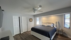 A bedroom with a bed, a ceiling fan, a window with blinds, and a door.