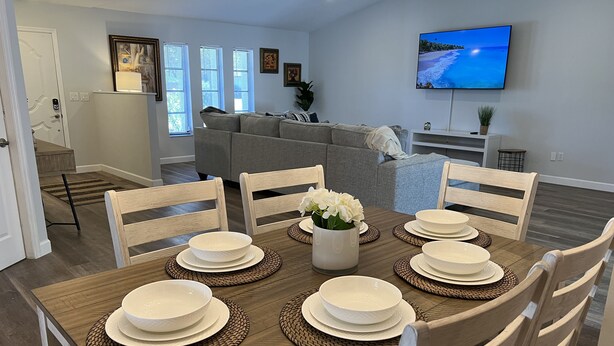 A dining area with a wooden table set for six, surrounded by white chairs.