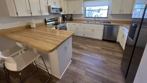 A modern kitchen with white cabinets, a wooden countertop, stainless steel appliances, and a window providing natural light.
