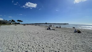 A beach with a pier extending into the ocean, sandy beach, and a clear sky.