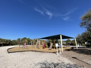 Children can play on slides, swings, and climbing frames under a shaded pavilion.