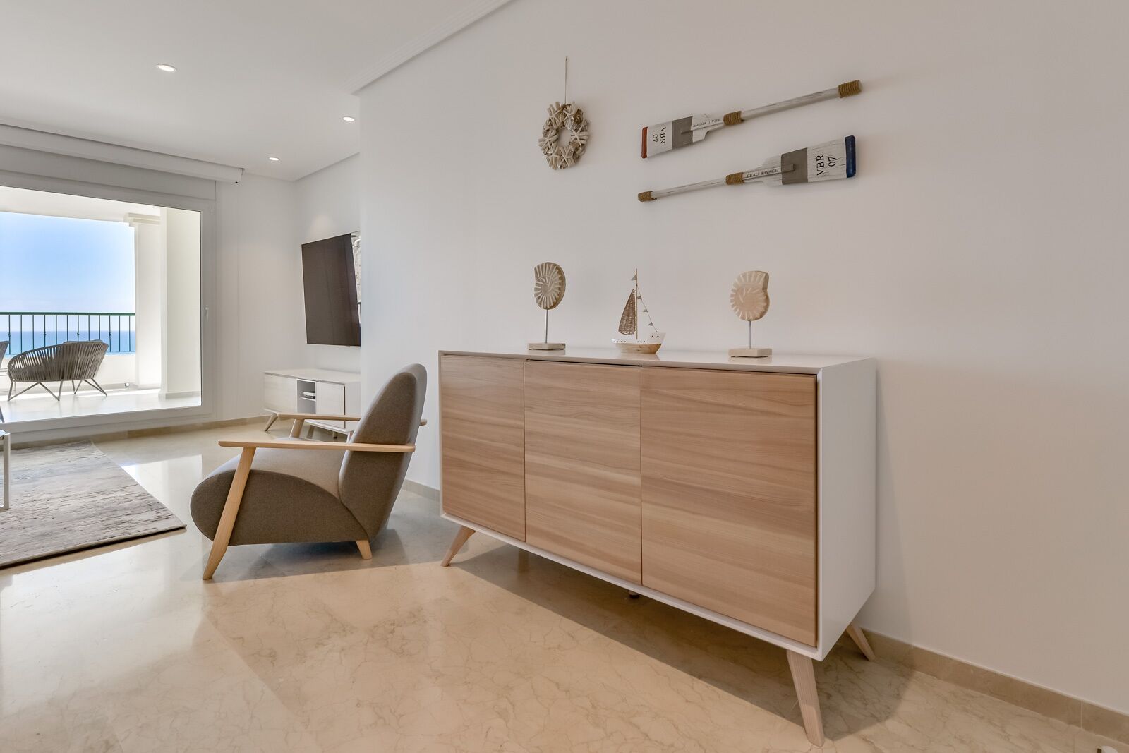 Un salon moderne avec un meuble en bois, un fauteuil et des objets décoratifs accrochés au mur.