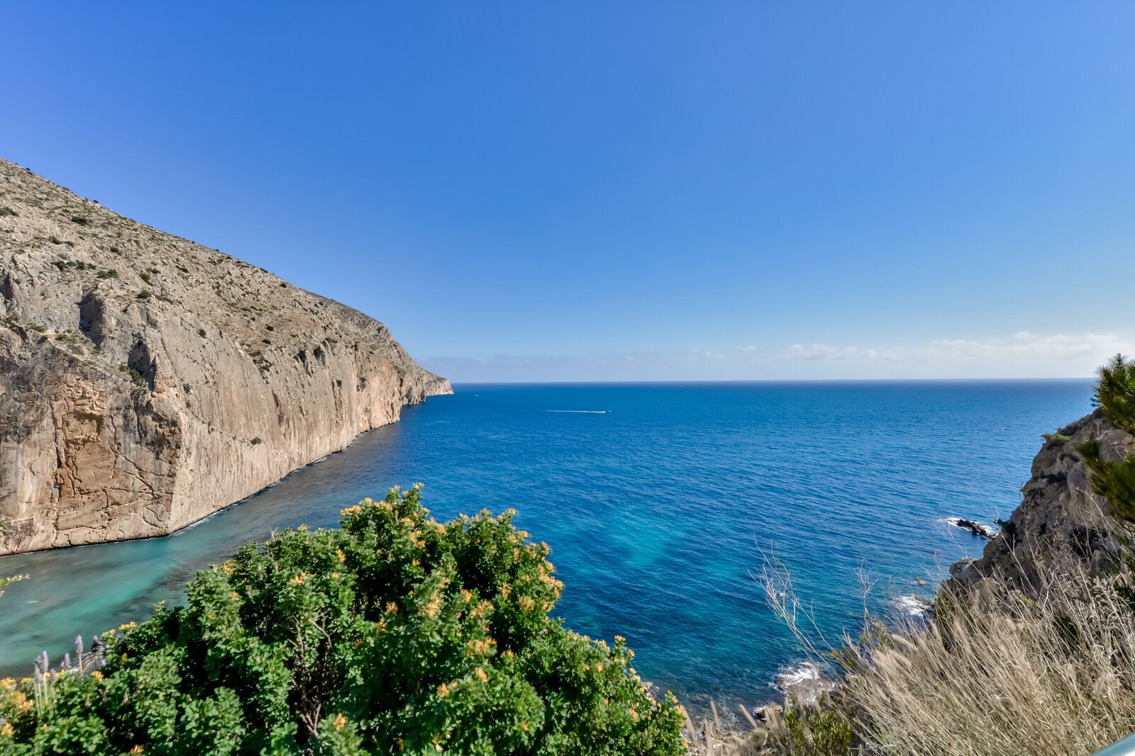 Un paisaje costero con un acantilado rocoso y un mar azul cristalino.