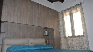 A bedroom with a bed, a wooden headboard, a shelf with books, and a window with curtains. - Balcony Bellavista B - Holiday home by the sea (Cefalù)