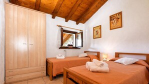 A bedroom with two beds, wooden wardrobe, a window with curtains, and a radiator.