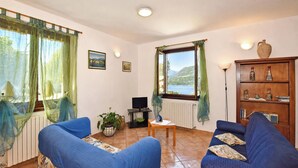 A living room with two blue sofas, a television, a table, a potted plant, and a view of a lake through a window.