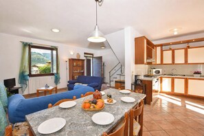 Zona pranzo con tavolo imbandito per quattro persone, un divano blu e una cucina sullo sfondo.