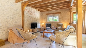 A cozy living room with a stone wall, wooden beams, a TV, wicker chairs, and a sofa.