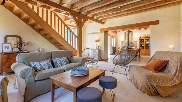A spacious living area with a wooden staircase, a sofa set, a dining table, and a chair.