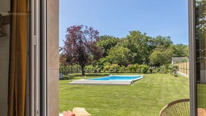 A view from a balcony with a swimming pool, a grassy lawn, and a wicker chair.