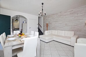 Een moderne eethoek met een witte tafel gedekt voor twee personen, een witte bank en een trap naar een hoger gelegen verdieping.