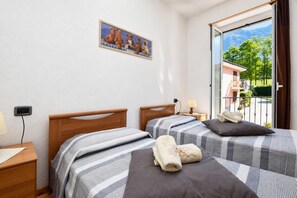 A bedroom with two beds, a painting on the wall, and a view of a balcony with a mountain in the background.