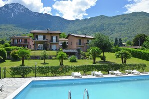A pool with lounge chairs, a mountain backdrop, and a large building with balconies.
