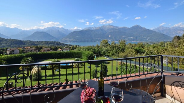 Un balcone con un tavolo apparecchiato per due, con vista su un paesaggio montuoso e un lago.