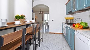 Una cucina moderna con zona pranzo, con isola centrale, sedie, un lampadario e vista attraverso un arco.