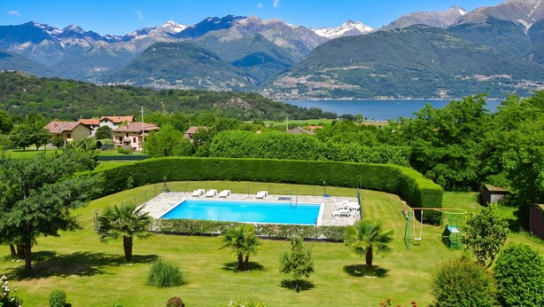 Une piscine entourée de pelouses et de haies bien entretenues, avec en arrière-plan des montagnes et un lac.