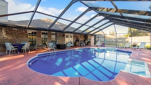 Una piscina cubierta con techo de vidrio, mobiliario exterior y pared de ladrillo.
